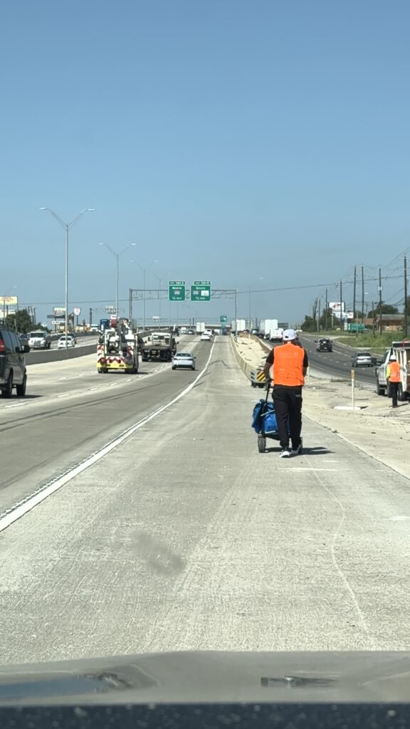 Coach Andrew walking the highway shoulder in a hi-vis vest, pulling his cart